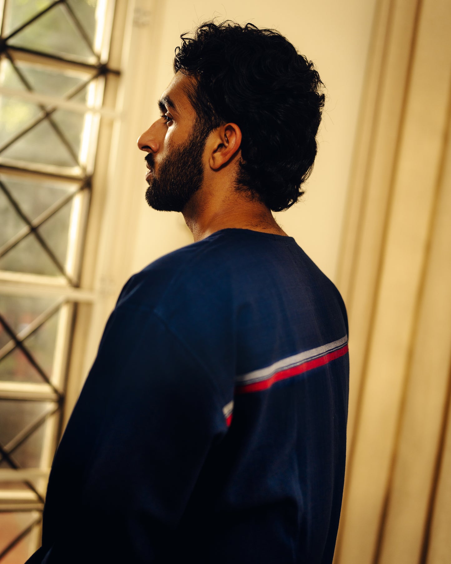 Man wearing a navy blue jacket with red and white stripes, standing indoors.