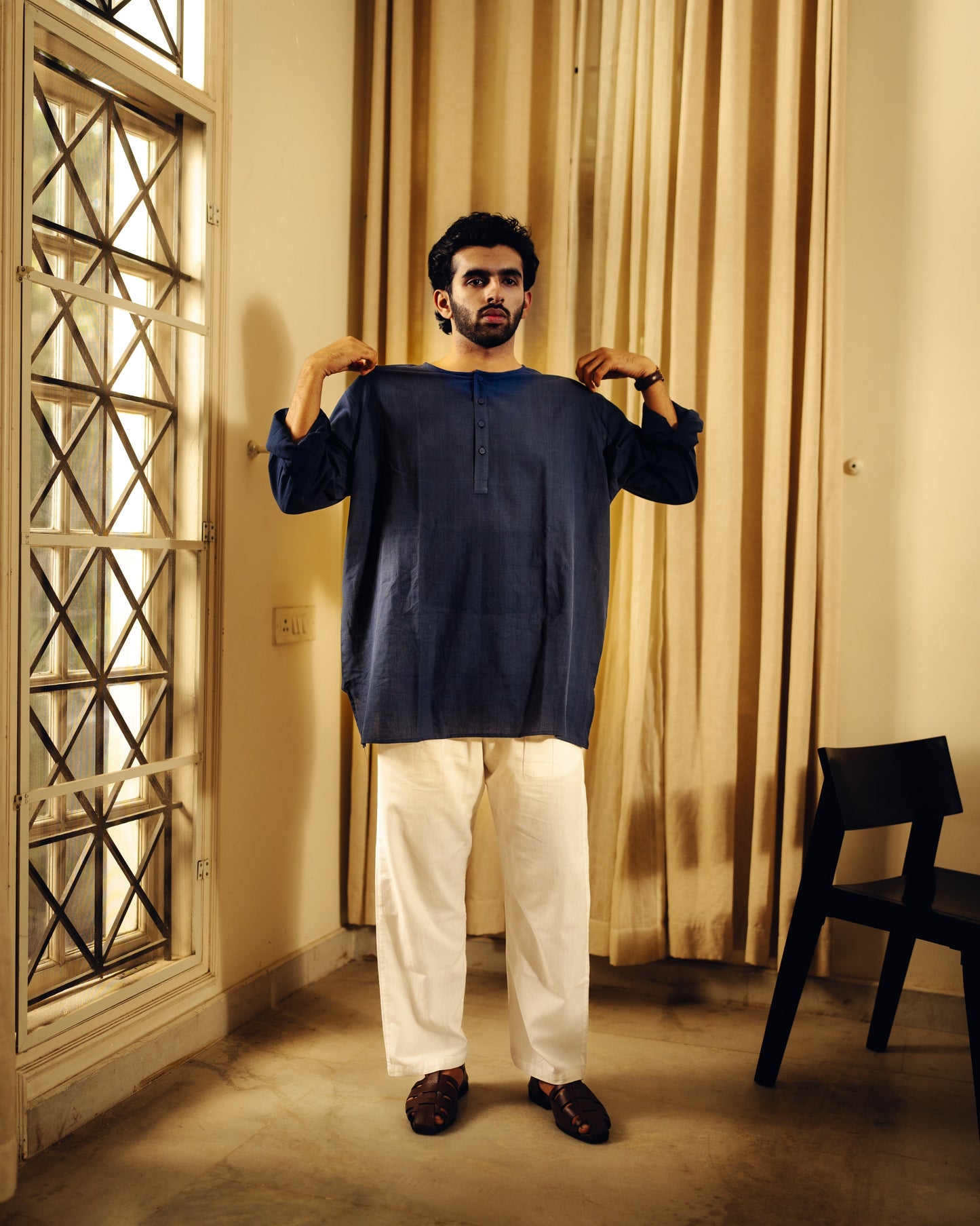 Man holding a dark blue Blueberry kurta in a room with curtains and a chair.