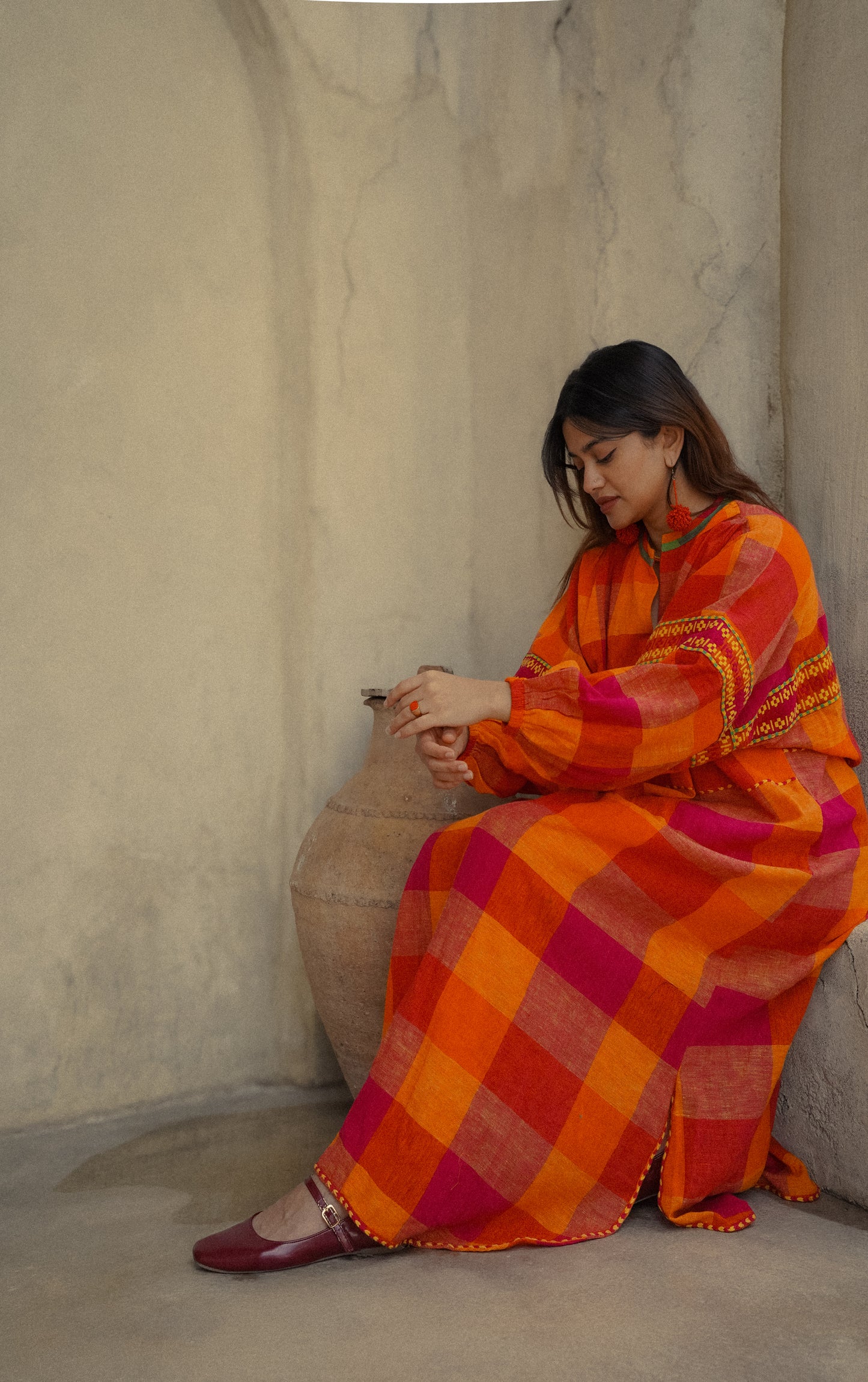 Woman in a colorful traditional outfit sitting against a textured wall.