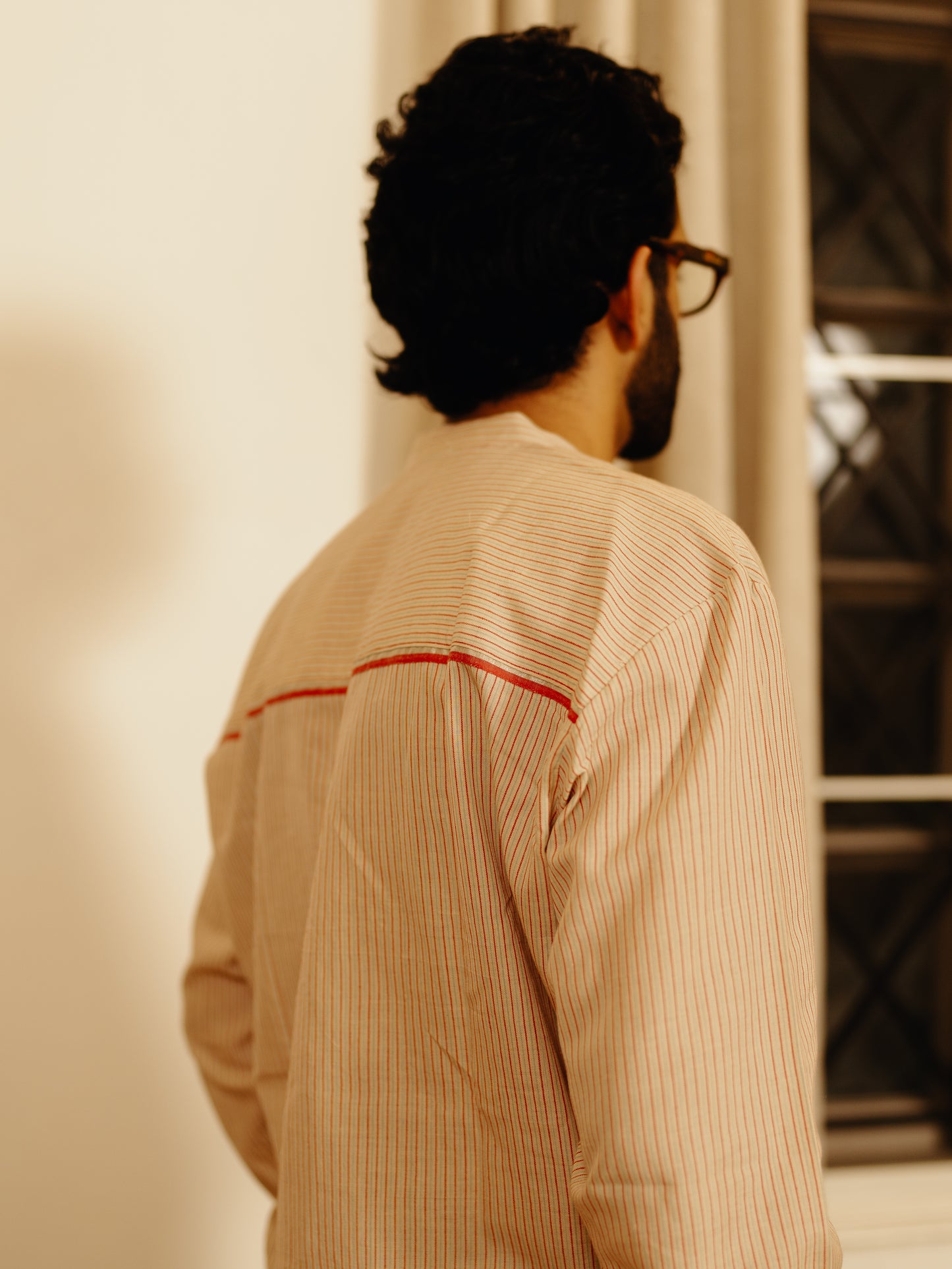 Man wearing a beige Sand striped shirt with red accents, standing indoors.