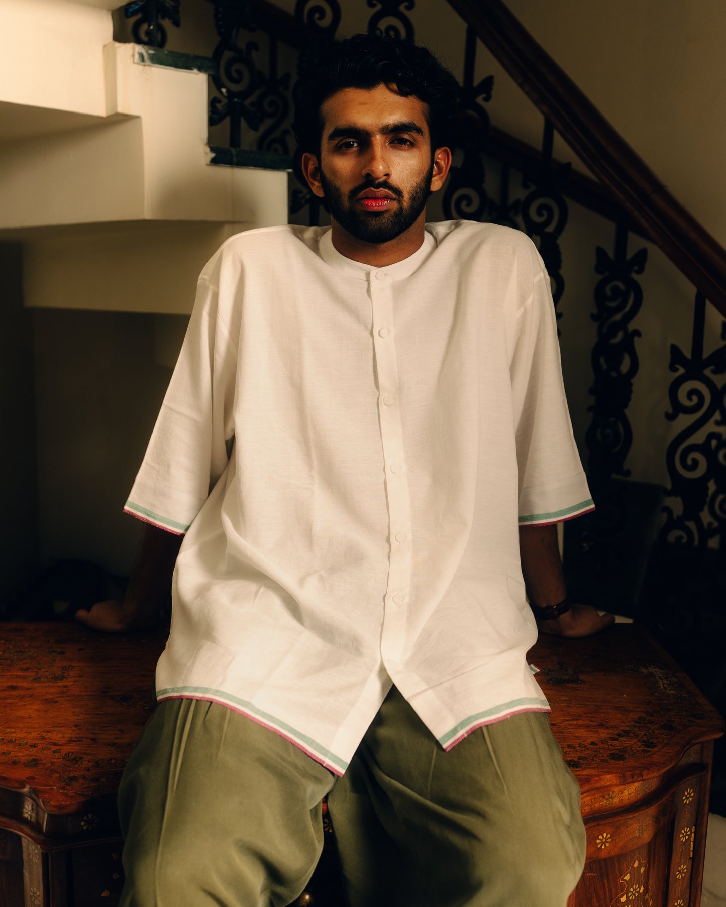 Man wearing a white shirt and green pants sitting on a wooden staircase.