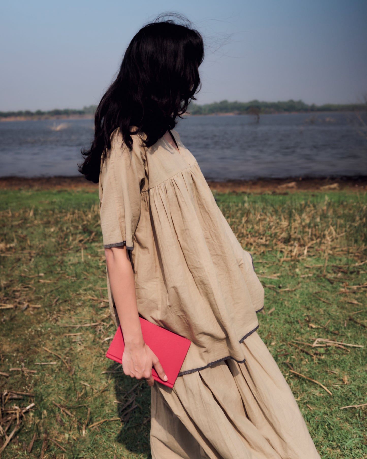 Woman in a beige dress holding a red book by a body of water