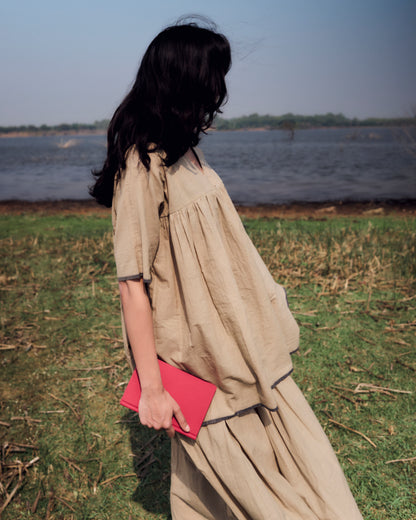 Woman in a beige dress holding a red book by a body of water
