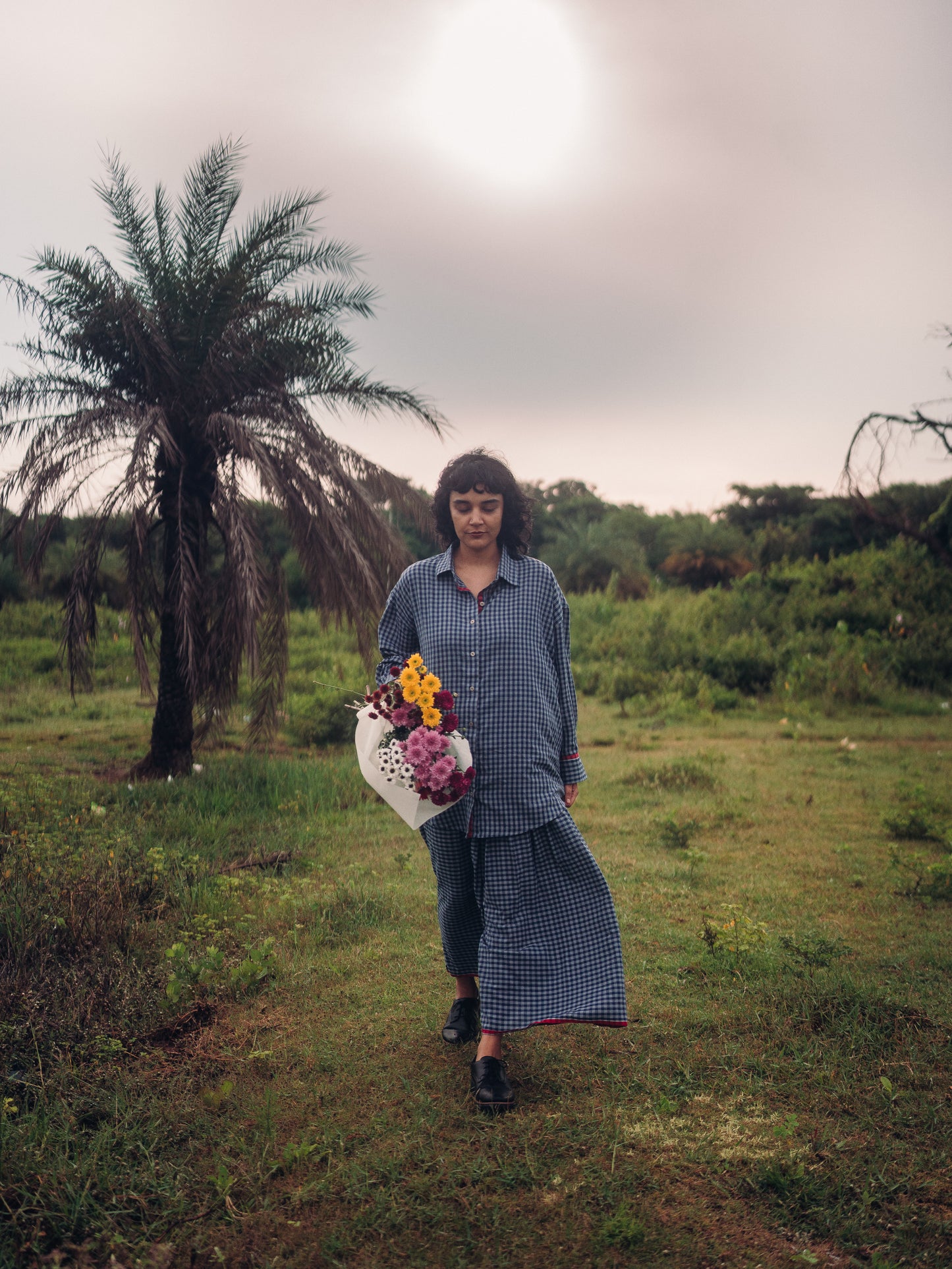 Person holding flowers in a grassy field with a palm tree