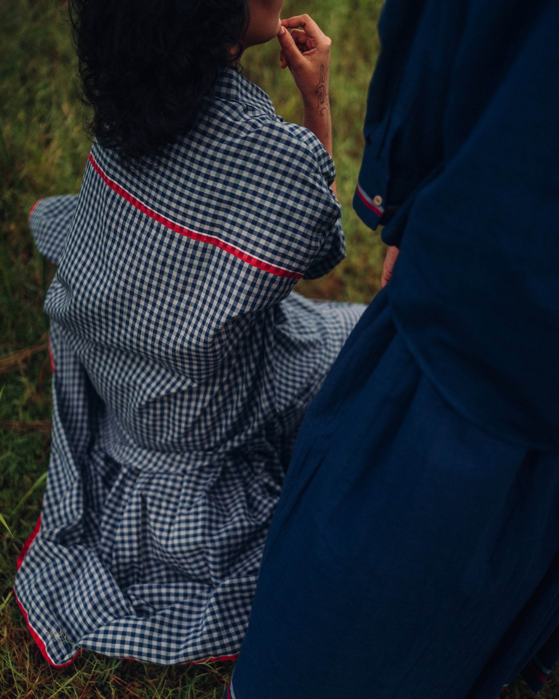 Person wearing a blue and white checkered dress sitting on grass