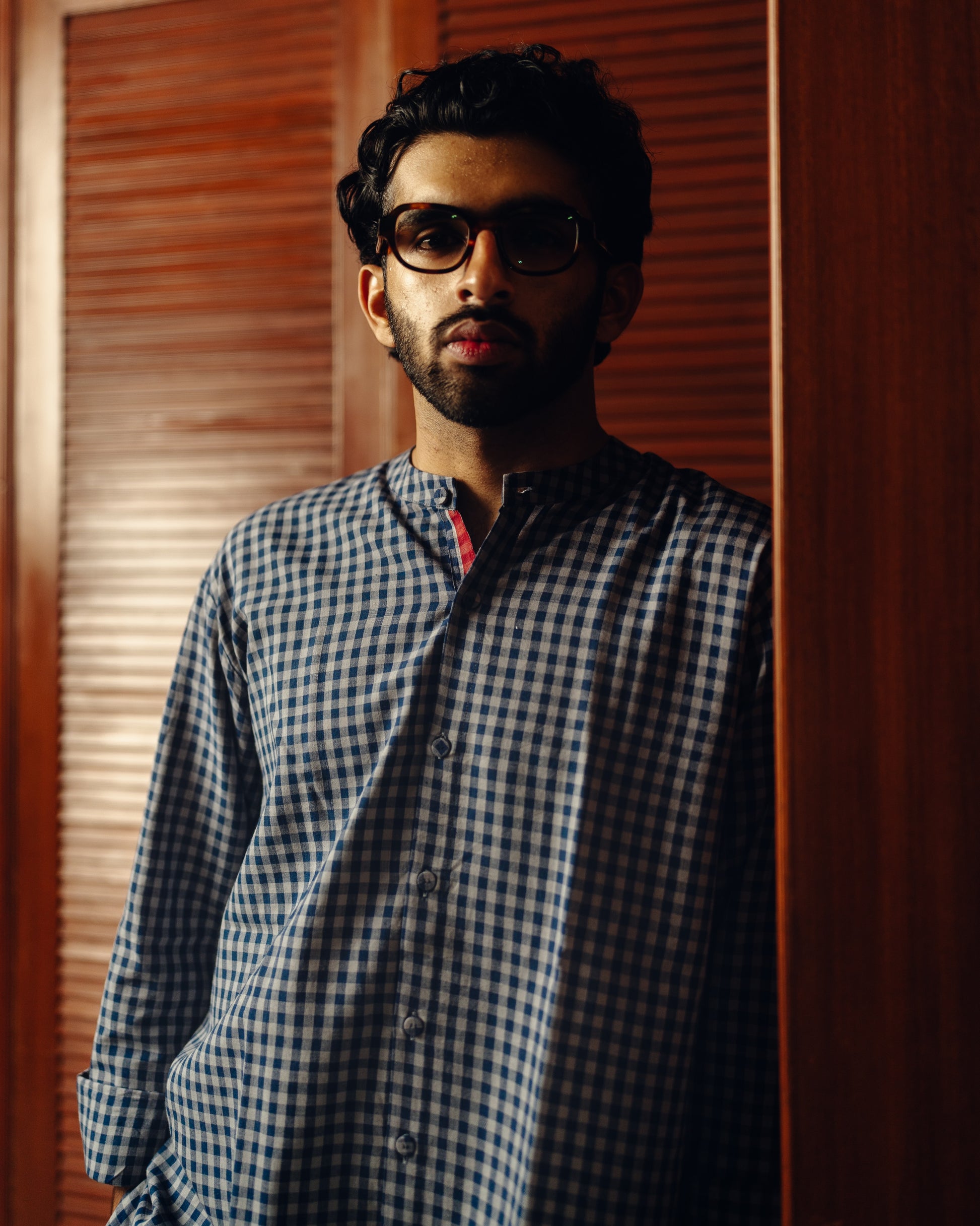 Man wearing a Blueberry checks - full sleeve shirt standing in a room with beige curtains and a window.