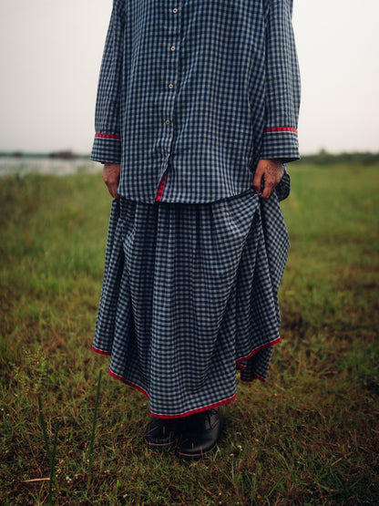 Person wearing a long, checkered dress standing in a grassy field.