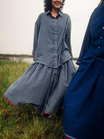 Woman in a blue checkered dress standing in a field with another person wearing a blue coat.