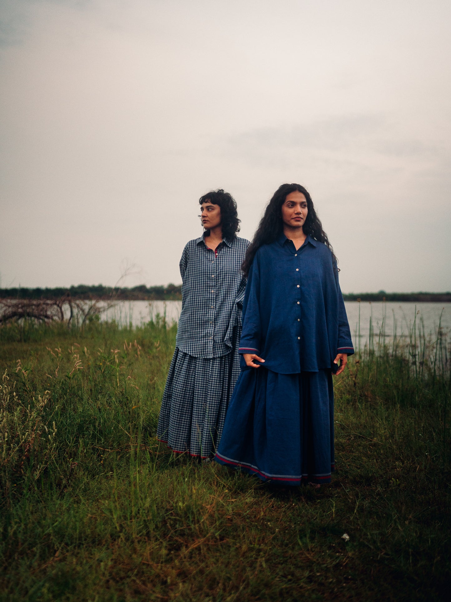 Two women standing in a grassy field with a body of water in the background