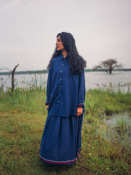 Woman in a blue outfit standing in a grassy area near a body of water.