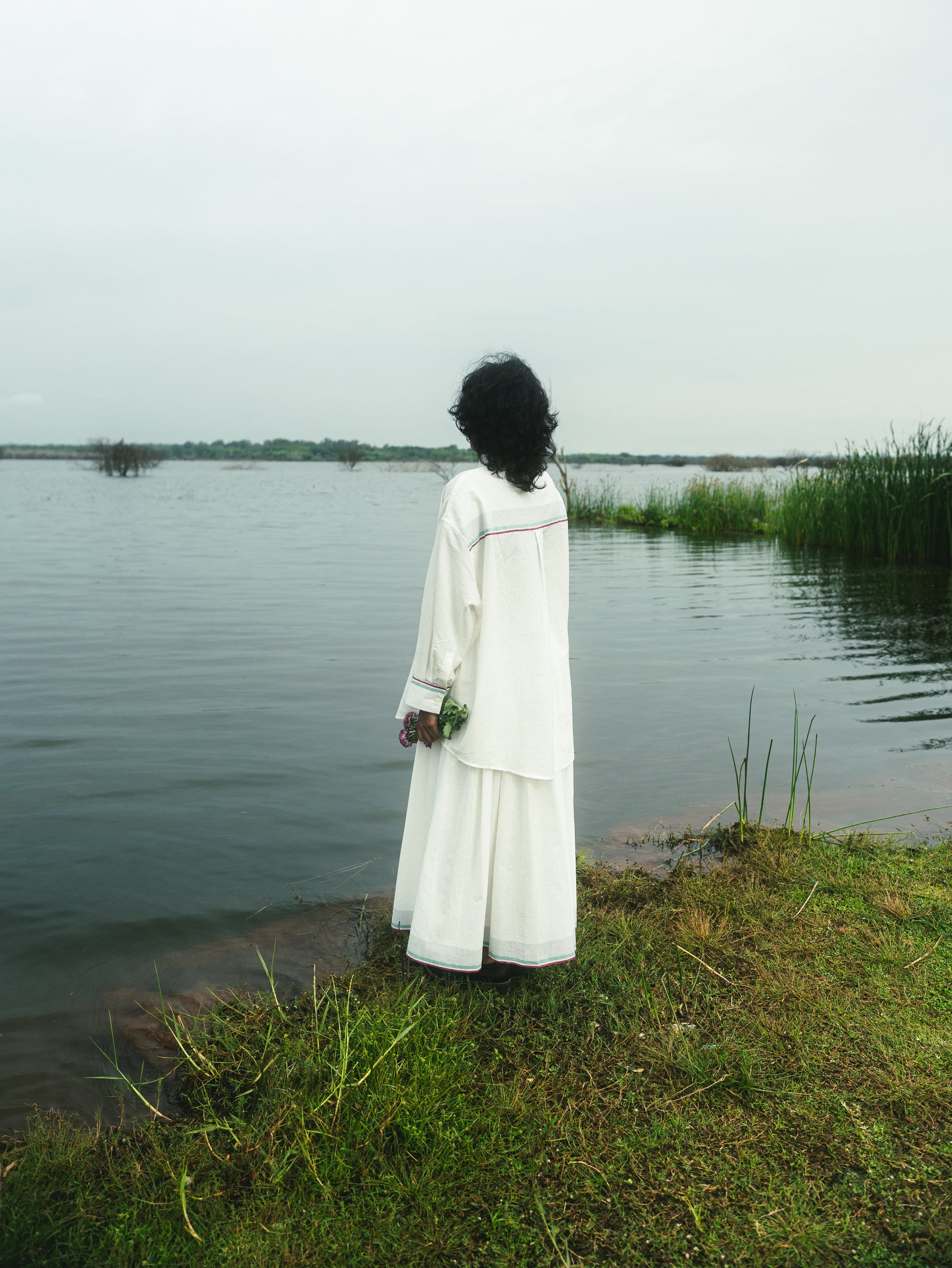Person in a white dress standing by a body of water