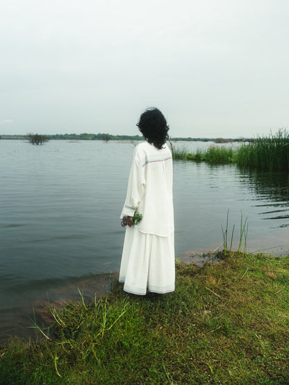 Person in a white dress standing by a body of water