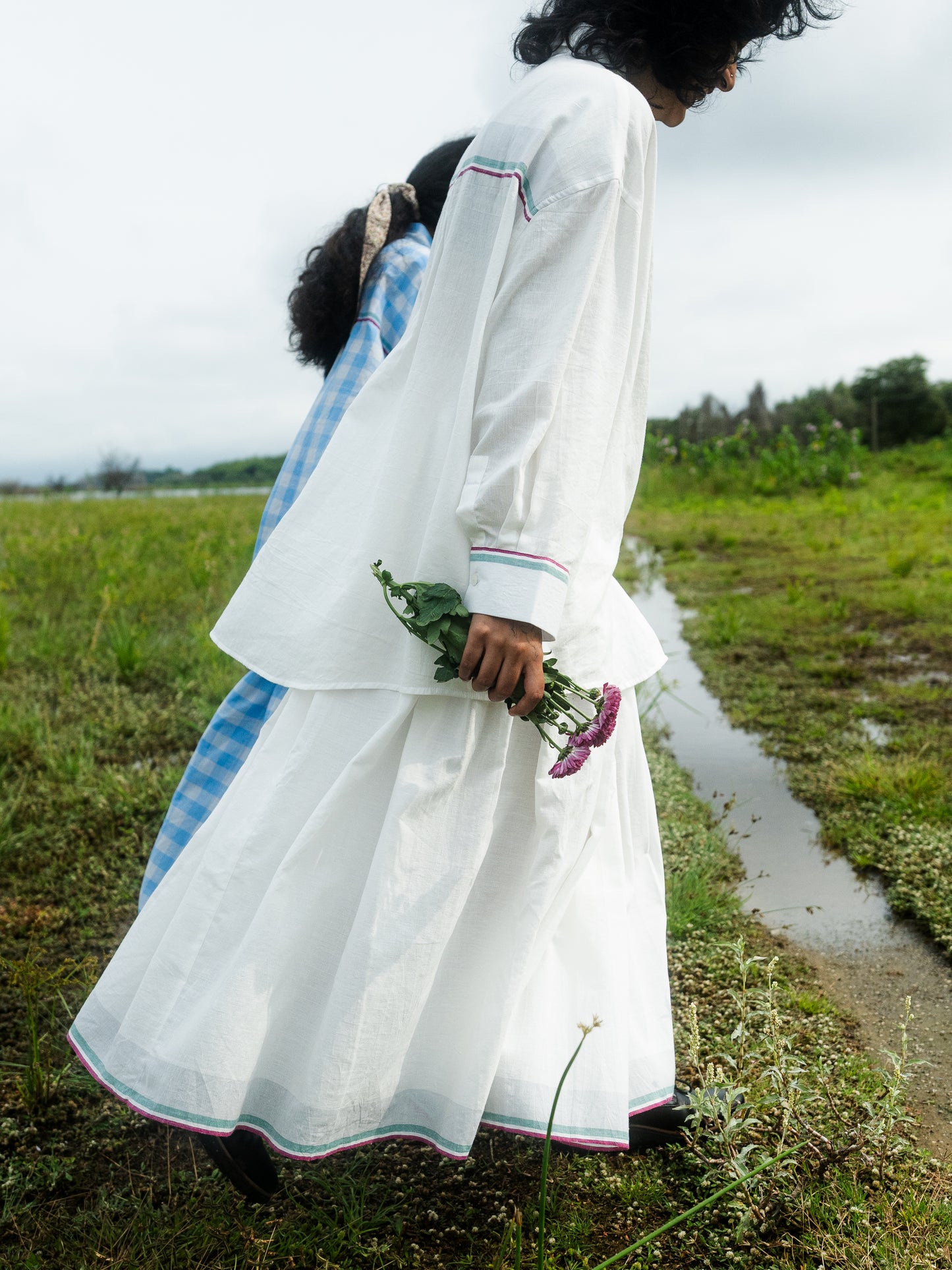 Woman in a white traditional outfit holding flowers in a grassy field