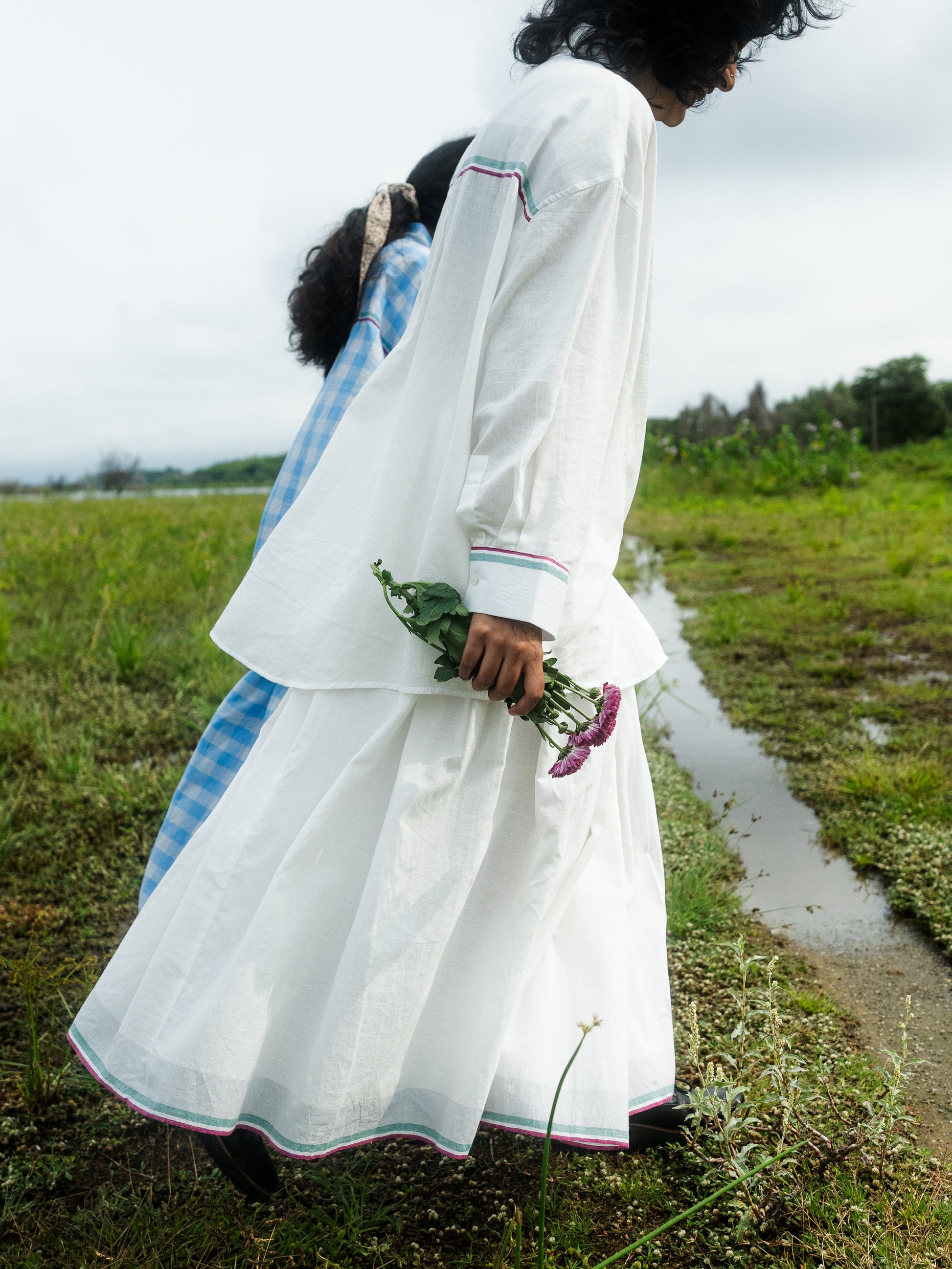 Woman in a white traditional outfit holding flowers in a grassy field