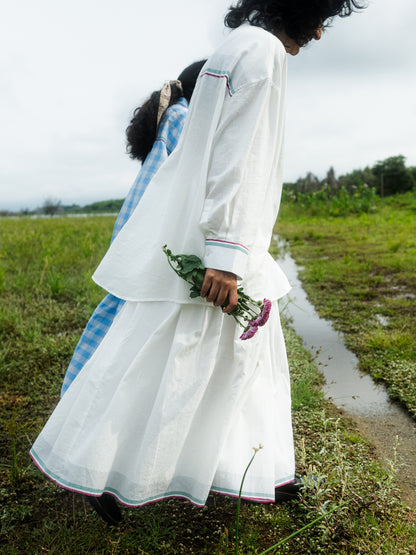 Woman in a white traditional outfit holding flowers in a grassy field