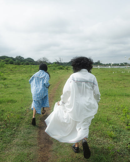 Two people walking away from the camera on a grassy path with a cloudy sky.