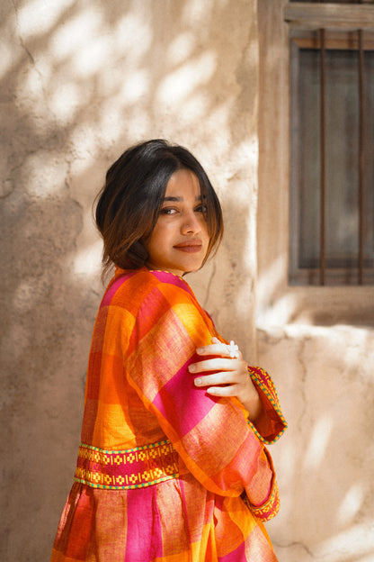 Woman wearing a colorful traditional outfit standing against a textured wall.