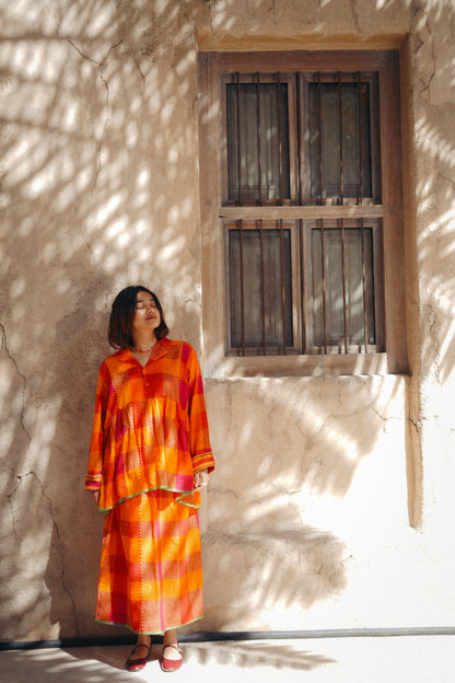 Woman in an orange dress standing in front of a textured wall with a window.
