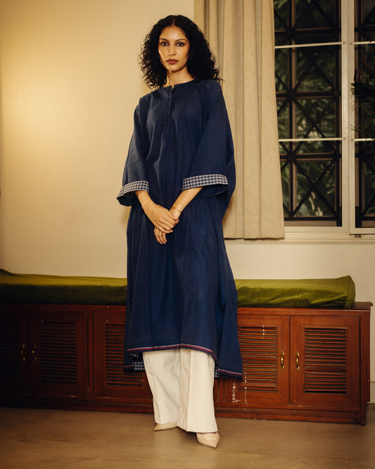 Woman wearing a navy blue Free Size Kurta - Blueberry Plain with white pants standing in a room with wooden furniture and a window.