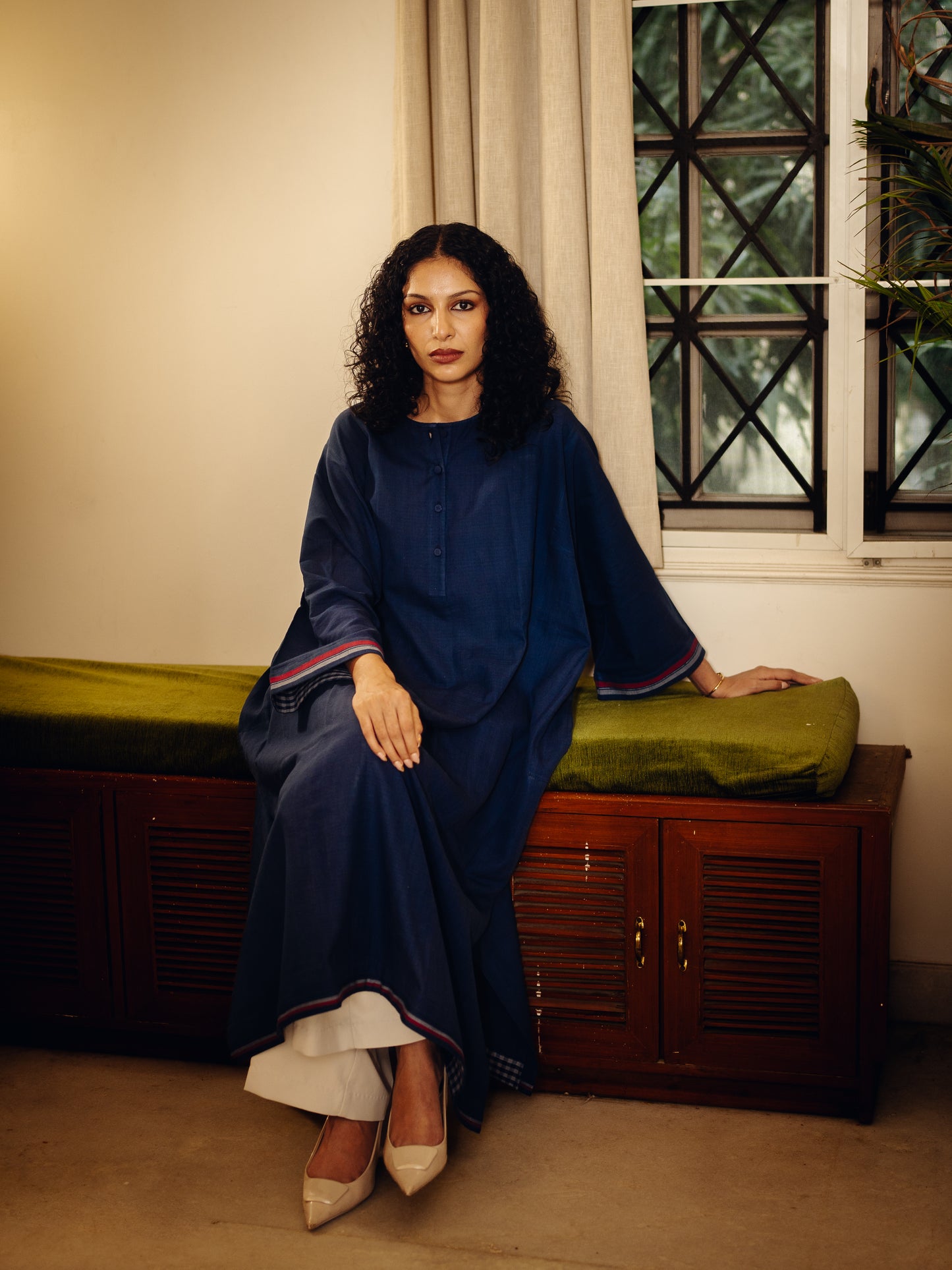 Woman in a blue dress Free Size Kurta - Blueberry Plain sitting on a wooden bench with green cushion in a room with a window.