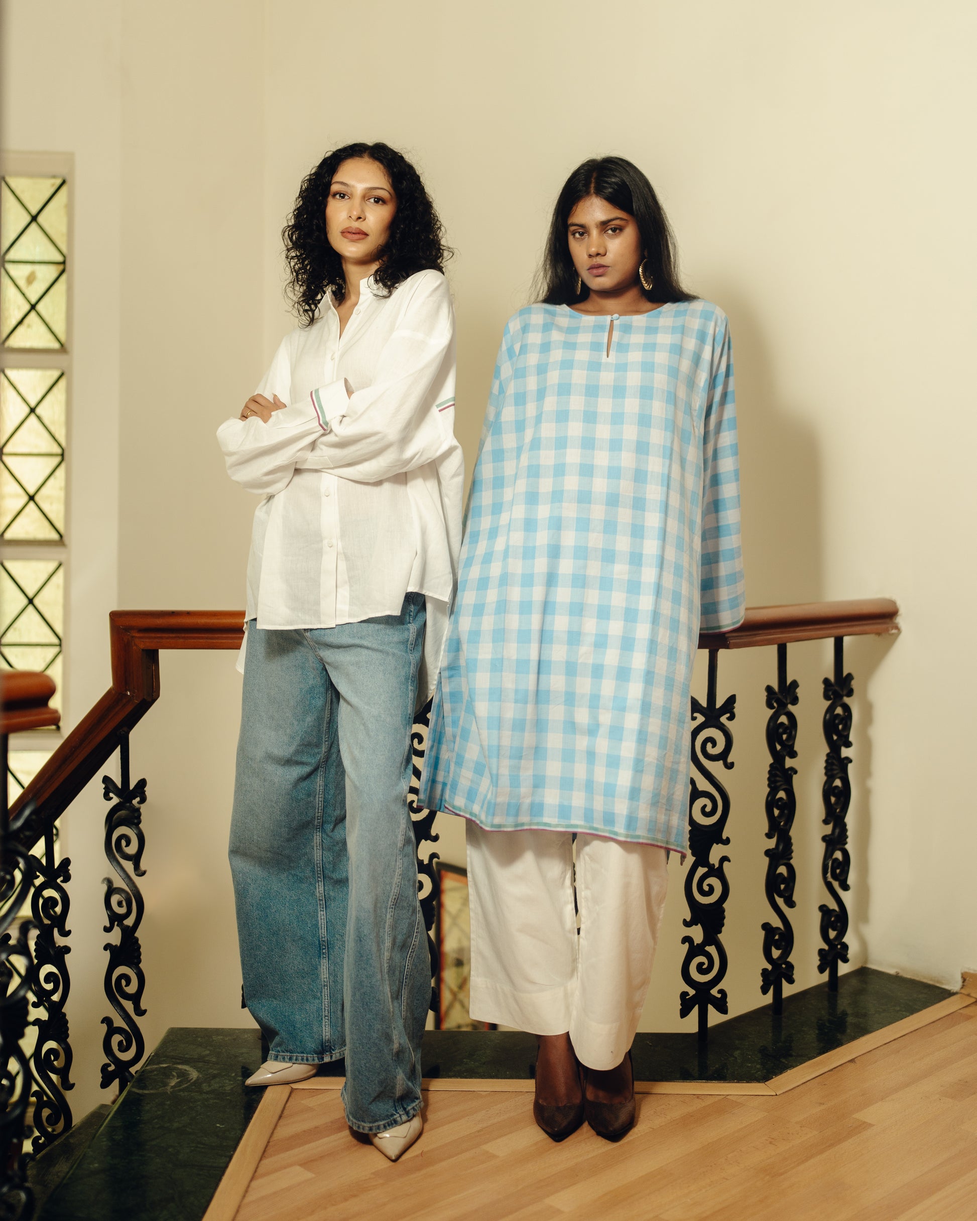 Two women standing on a staircase wearing light blue and white outfits.