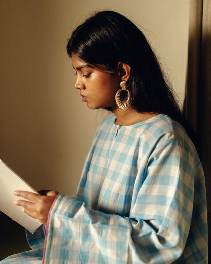 Woman in a Free size kurta - Light blue checks reading a book against a neutral background