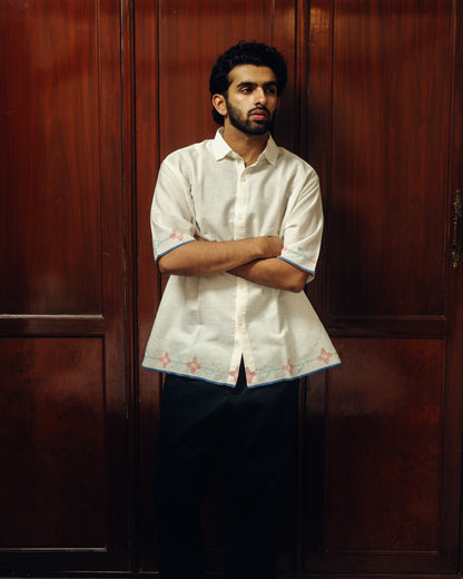 Man wearing a white embroidered shirt against a wooden background