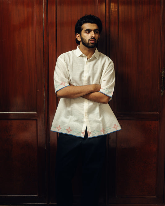 Man wearing a white embroidered shirt against a wooden background