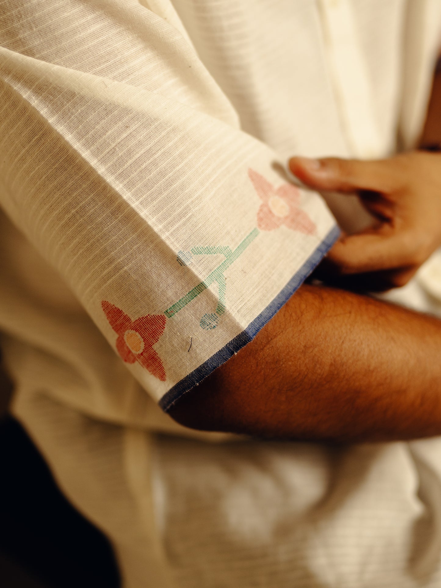 Close-up of a person wearing a white garment with floral embroidery on a dark background
