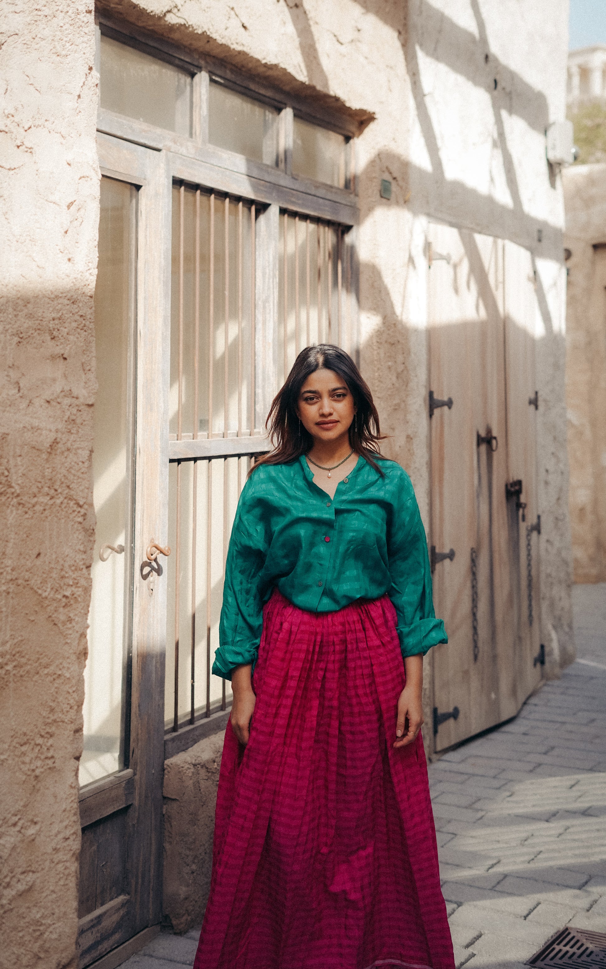 Woman in a green top and red skirt standing in front of a textured wall.