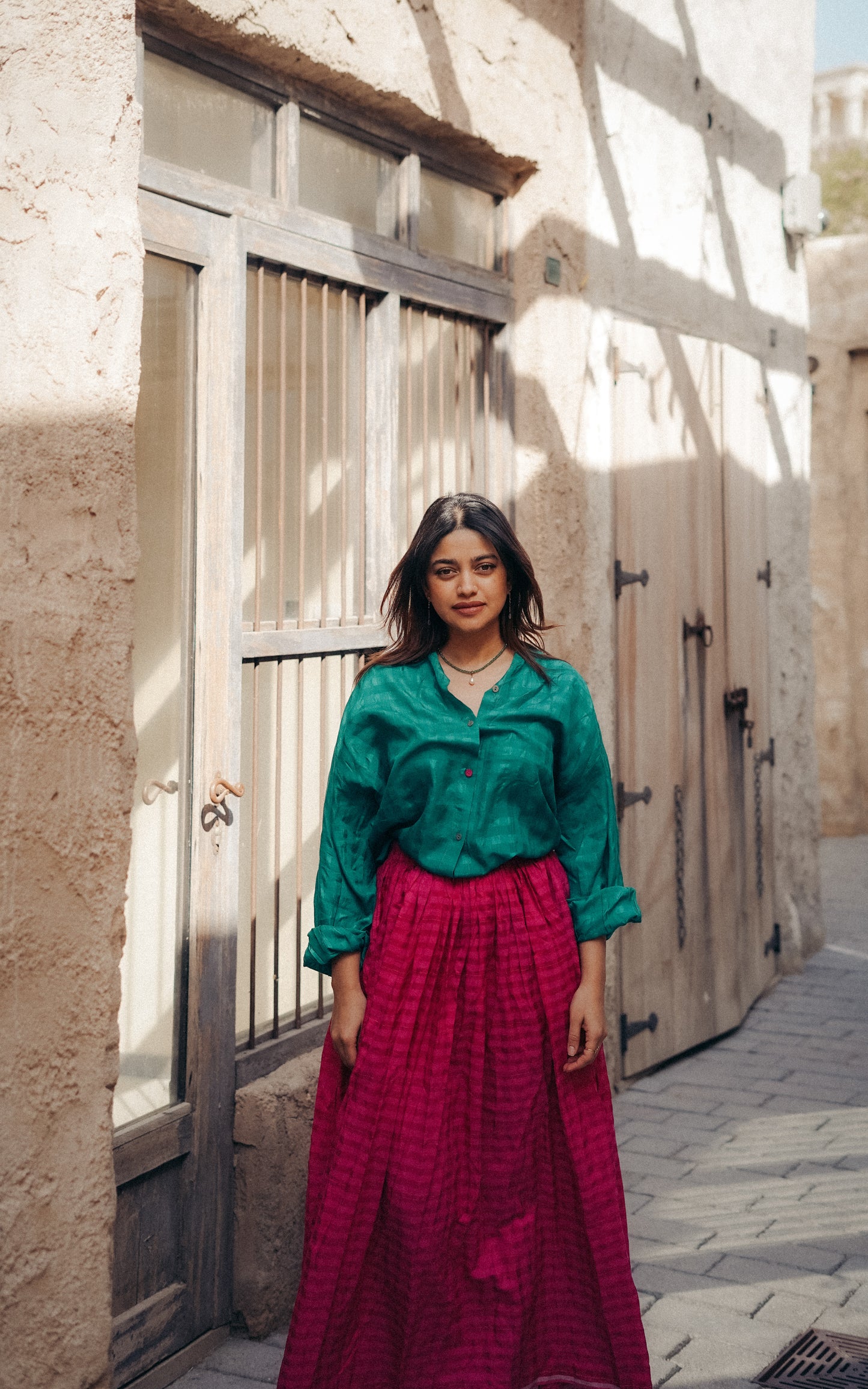 Woman in a green top and red skirt standing in front of a textured wall.