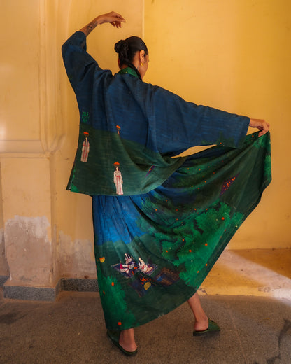Person wearing a traditional green and blue embroidered outfit against a yellow wall.