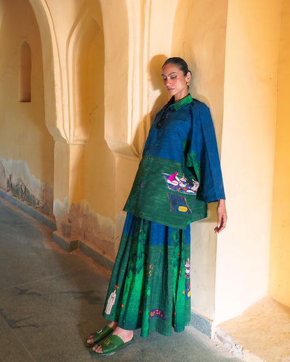 Woman in a green traditional outfit standing against a beige wall with arches.