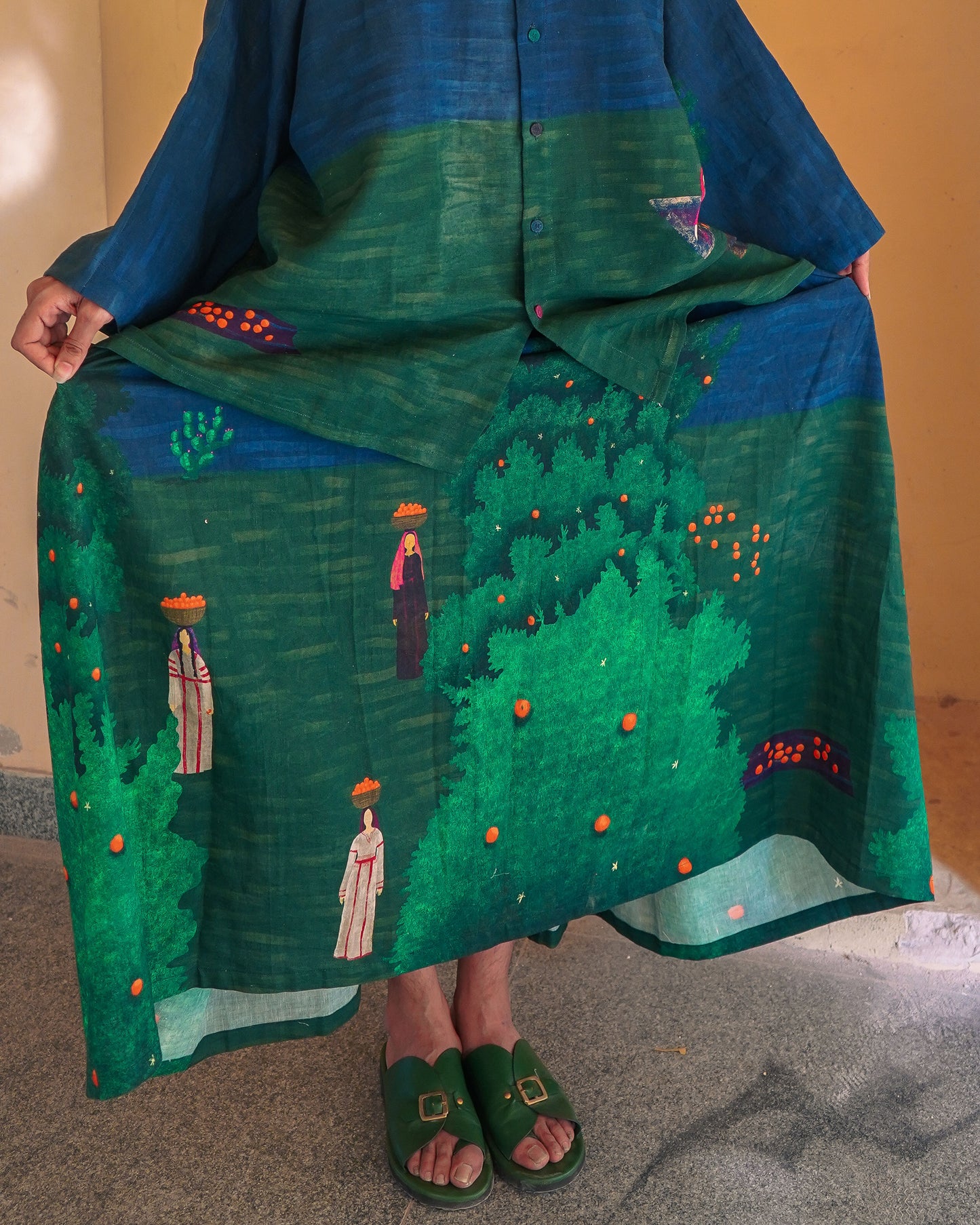 Person wearing a green embroidered skirt with a blue top against a neutral background