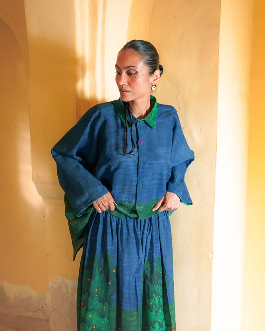 Woman wearing a blue and green traditional outfit against a yellow wall.