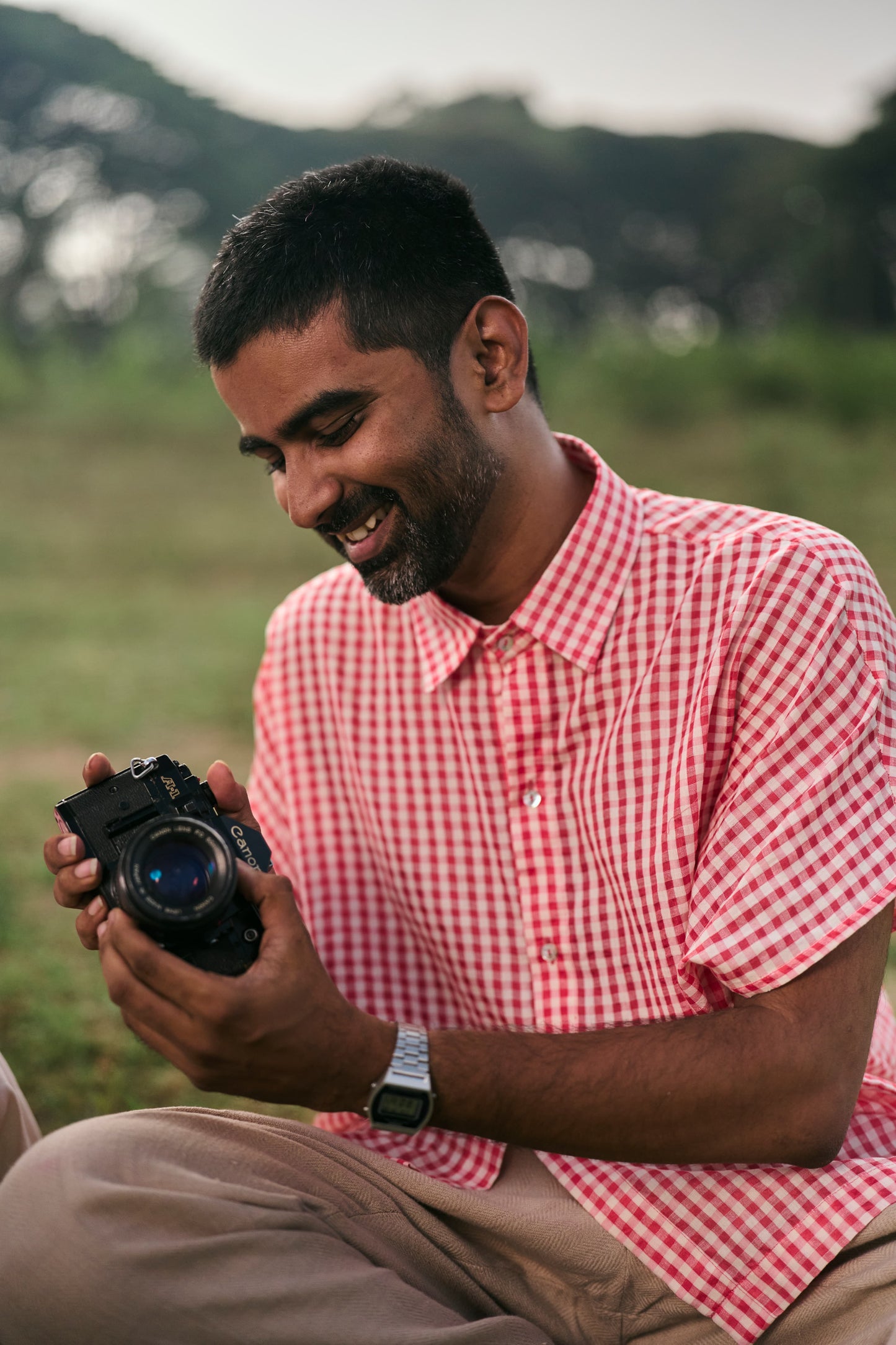 Man in a red checkered shirt holding a camera in a natural setting