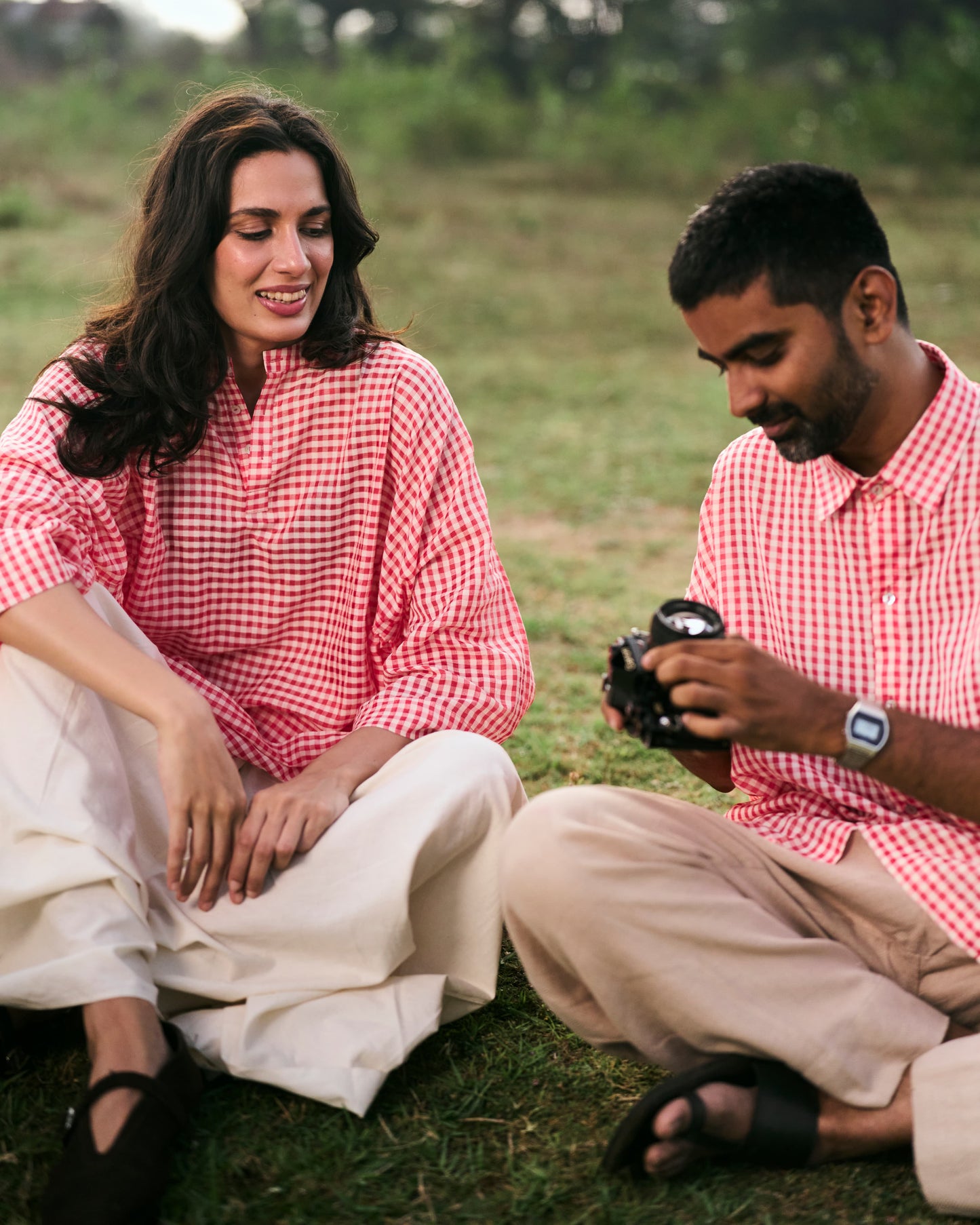 Two people sitting on the grass, one holding a camera.