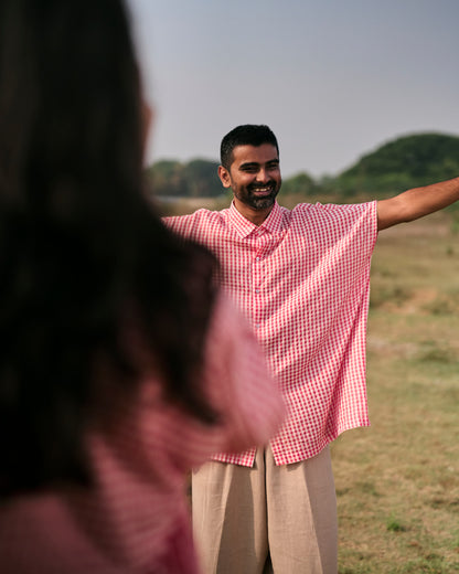 Man in a red checkered shirt standing in an open field with arms outstretched