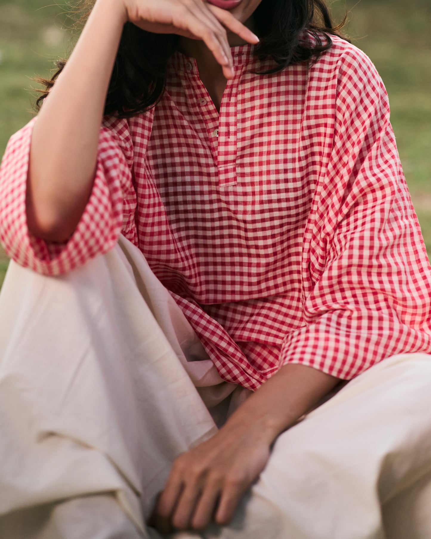 Person wearing a red and white checkered shirt sitting outdoors.