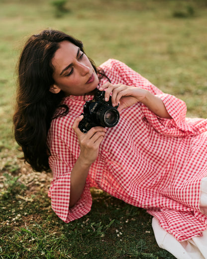 Woman in a red checkered dress holding a camera on grass
