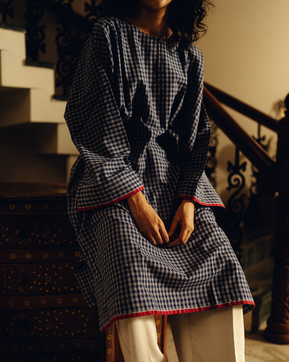 Person wearing a blue and white checkered dress with red trim, sitting on a staircase.