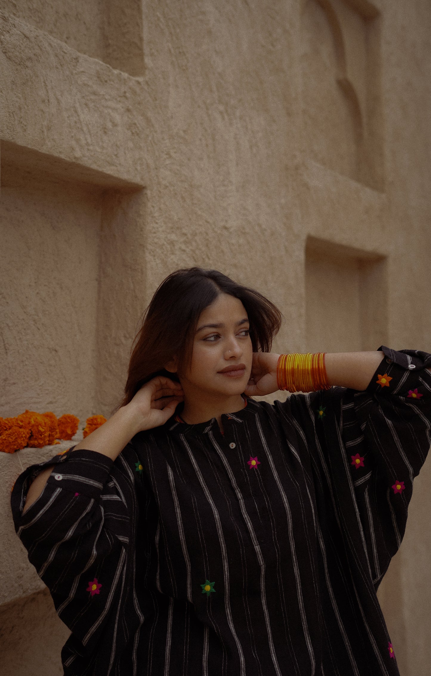 Woman in a black outfit with colorful accents against a beige wall.