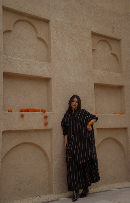 Woman in a black dress standing against a beige wall with arched niches.