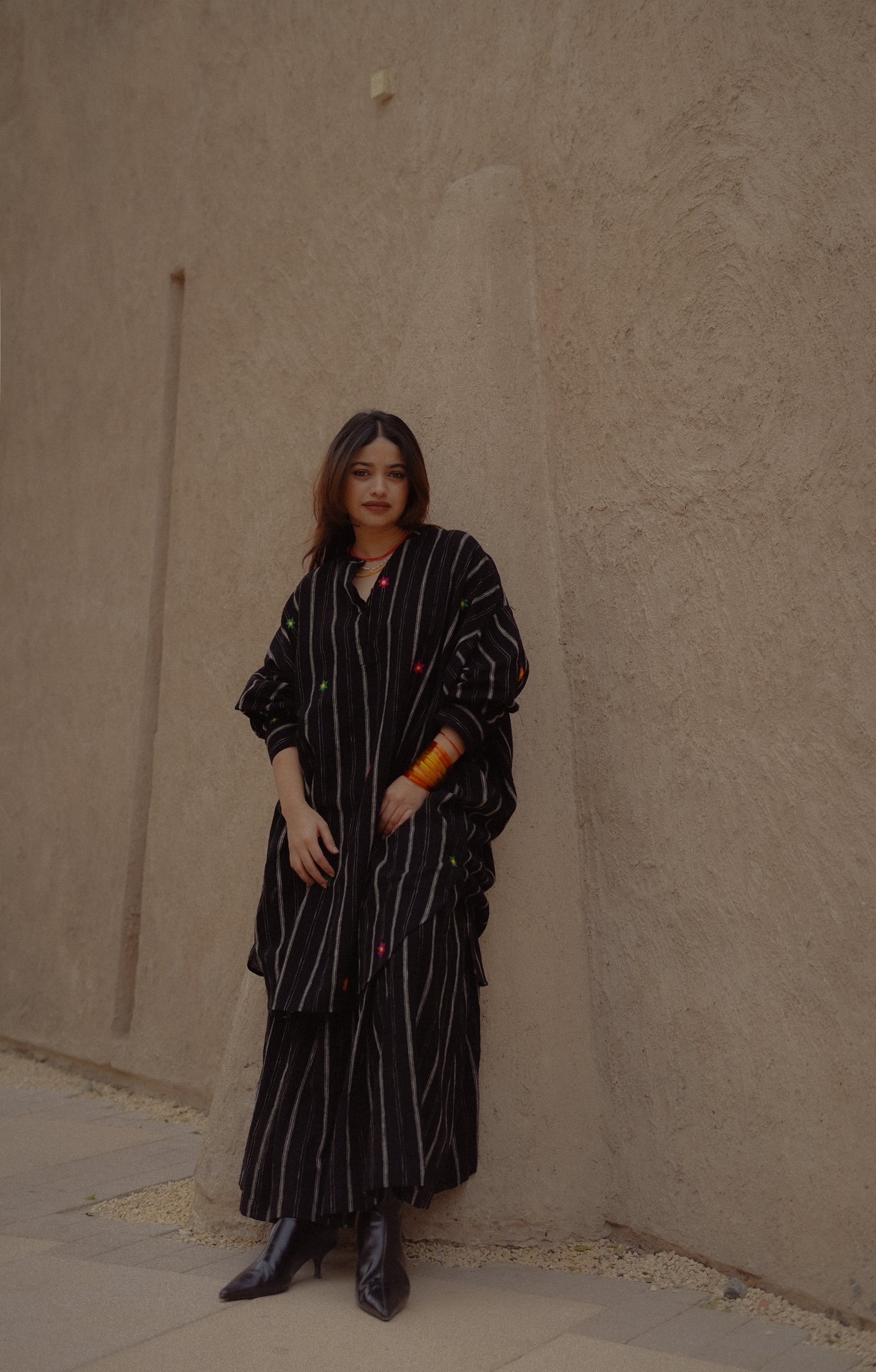 Person wearing a black pinstripe outfit against a beige wall.