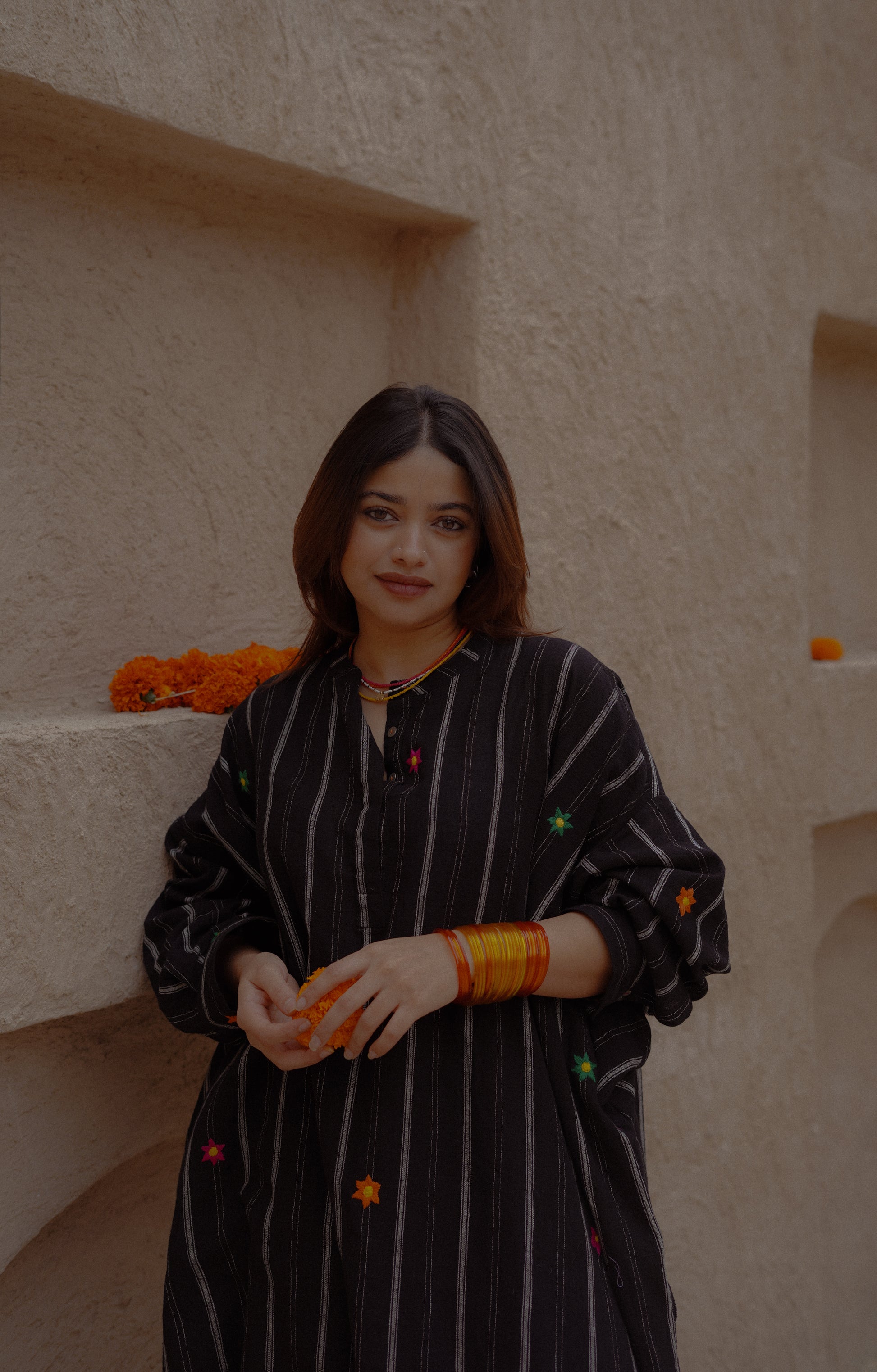 Woman in a black and white striped dress standing against a textured wall with orange flowers.