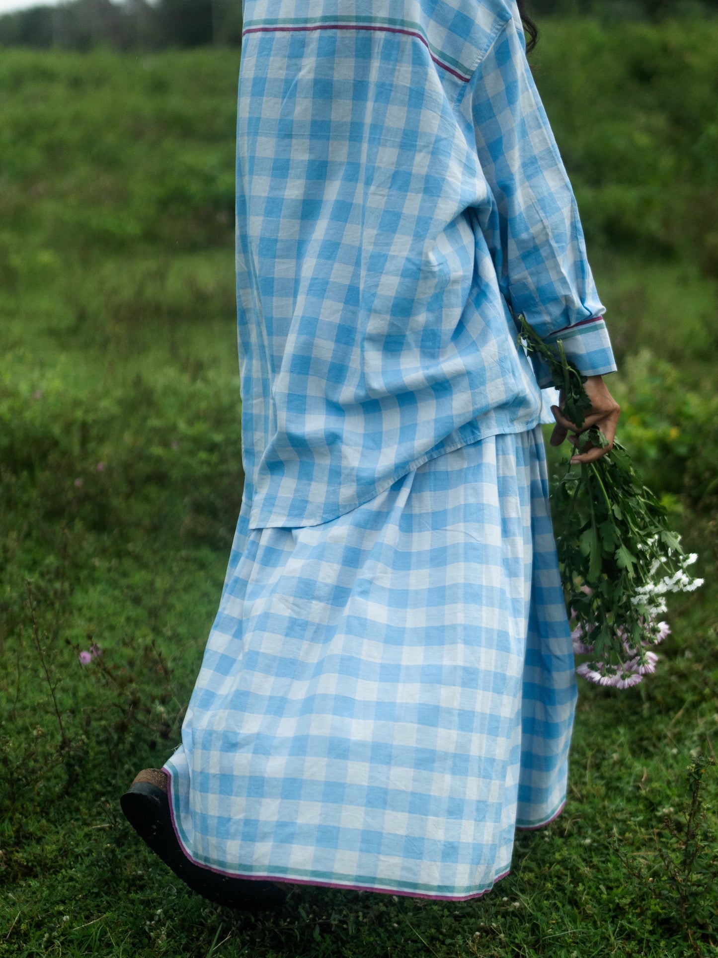 Person wearing a blue checkered outfit standing in a grassy field