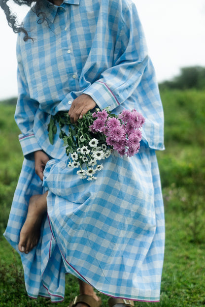 Person wearing a blue checkered dress holding flowers in a field