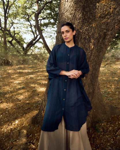 Woman in a dark blue shirt and beige pants standing next to a tree in a forest setting
