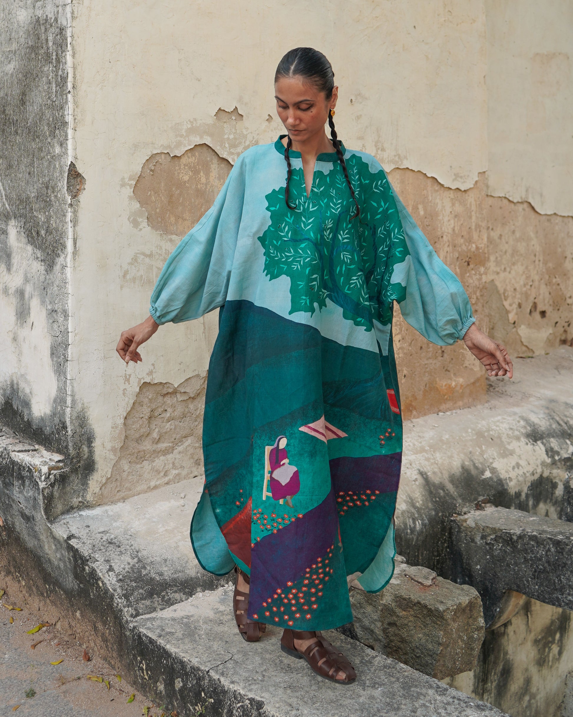 Woman in a colorful dress standing on stone steps with a textured wall background