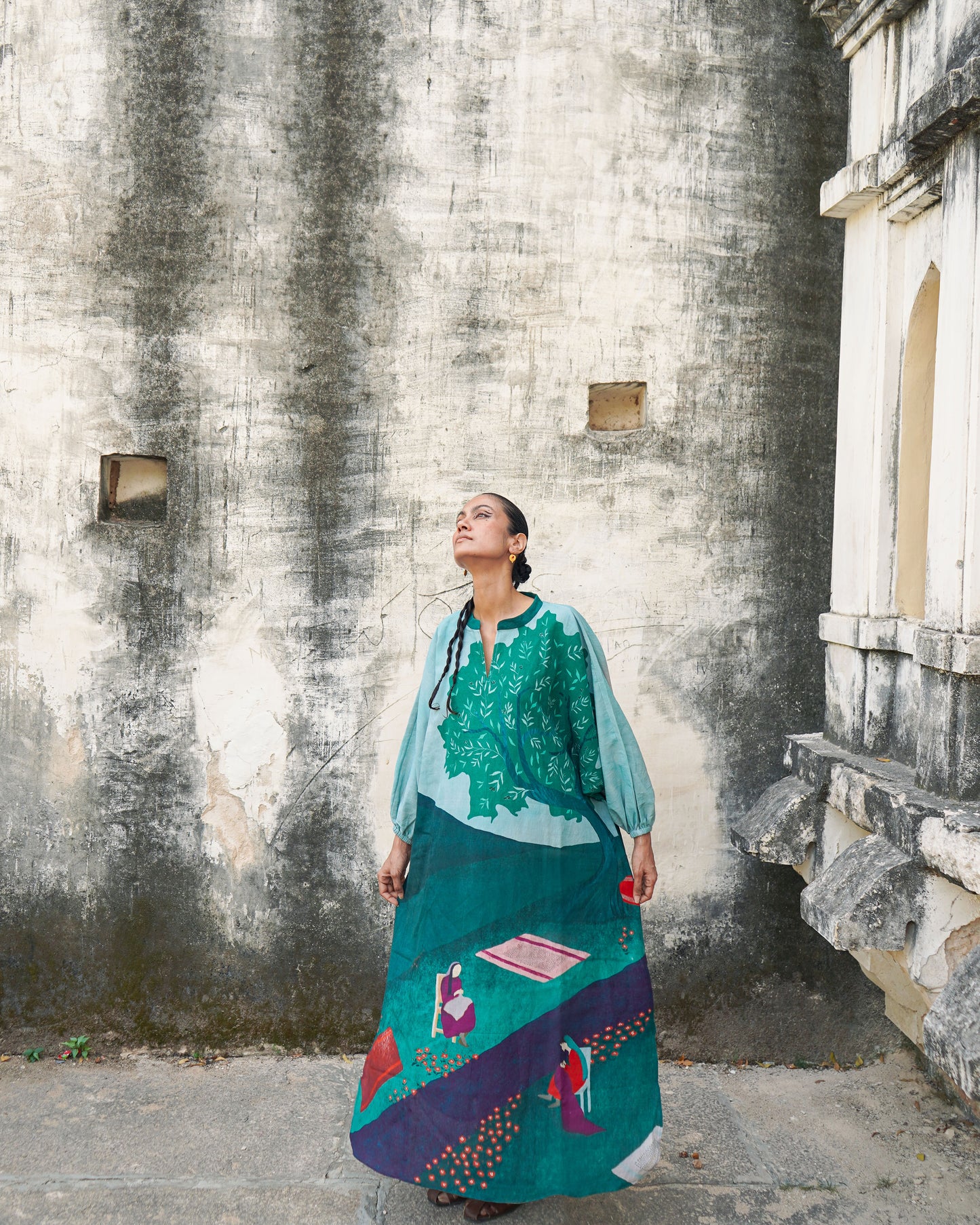 Woman in a colorful dress standing against a textured wall.
